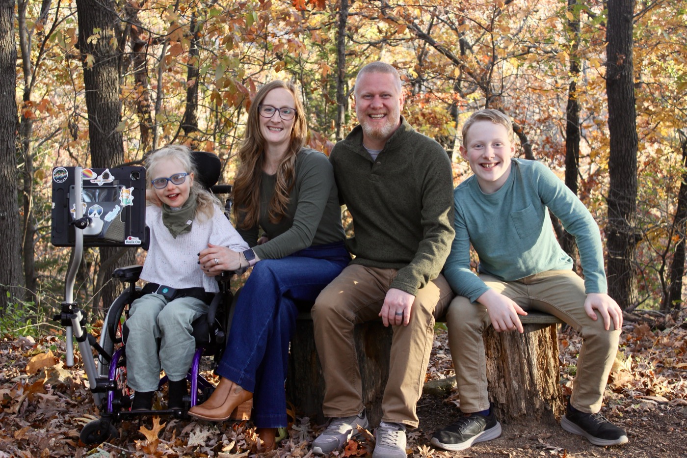 Adam Michael Roach and his family sitting together on a wooded trail in the fall